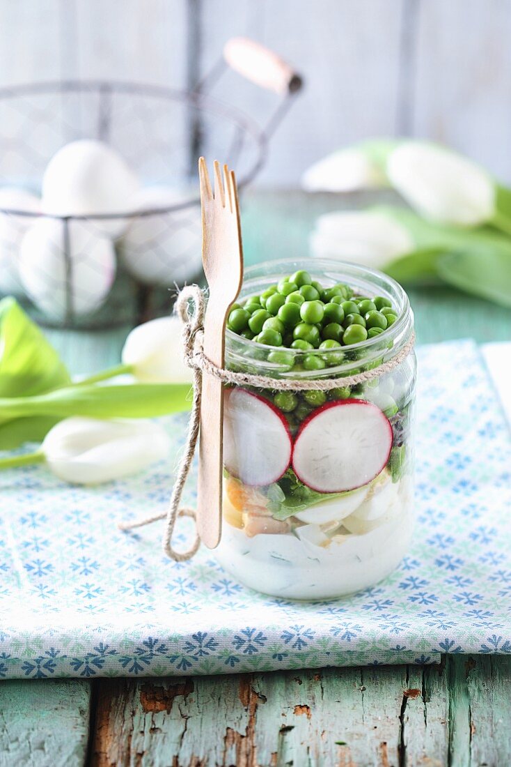 A spring salad in a glass jar with peas, radishes and egg