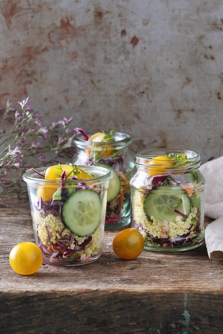 Millet salad in glass jars with cucumber, yellow cherry tomatoes and red cabbage