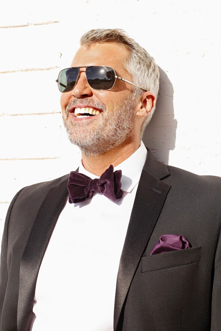 A man with grey hair wearing a white shirt, a blazer and a purple bow tie