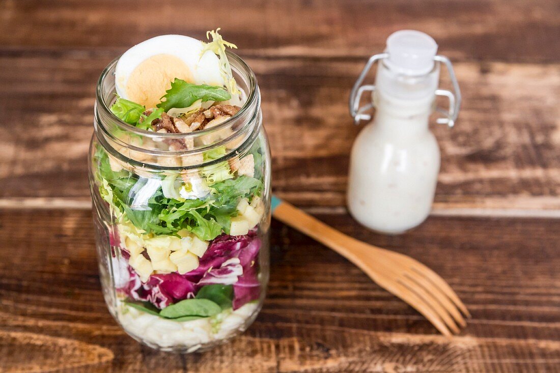 Orzo pasta with lambs lettuce, radicchio, endive, croutons, cheese, walnuts and eggs in a glass jar with dressing and a wooden fork