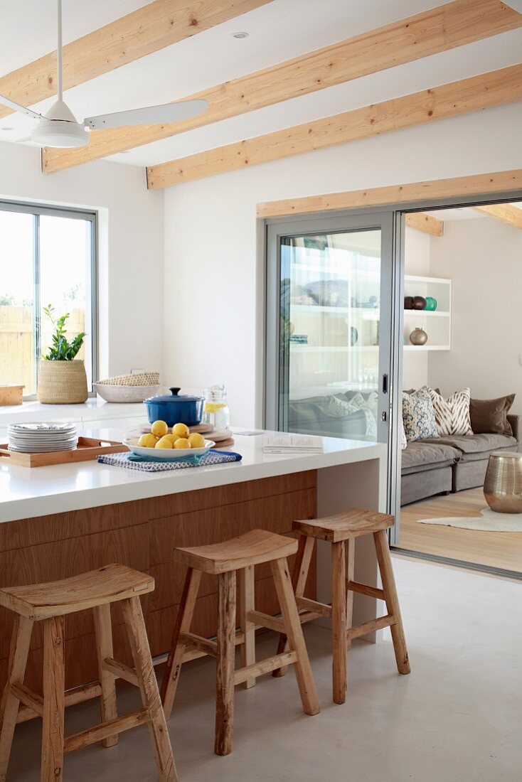 Rustikale Barhocker an weißer Küchentheke und Blick in Wohnbereich