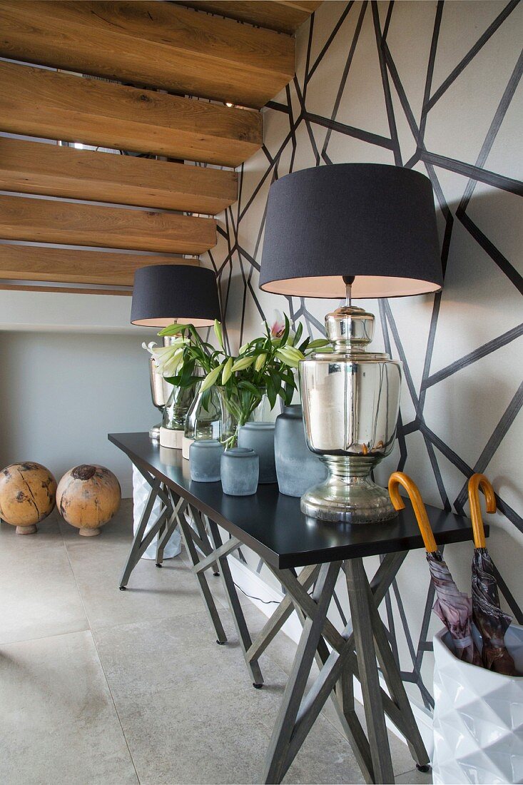 Elegant table lamps on black console table in hallway against black and white wall