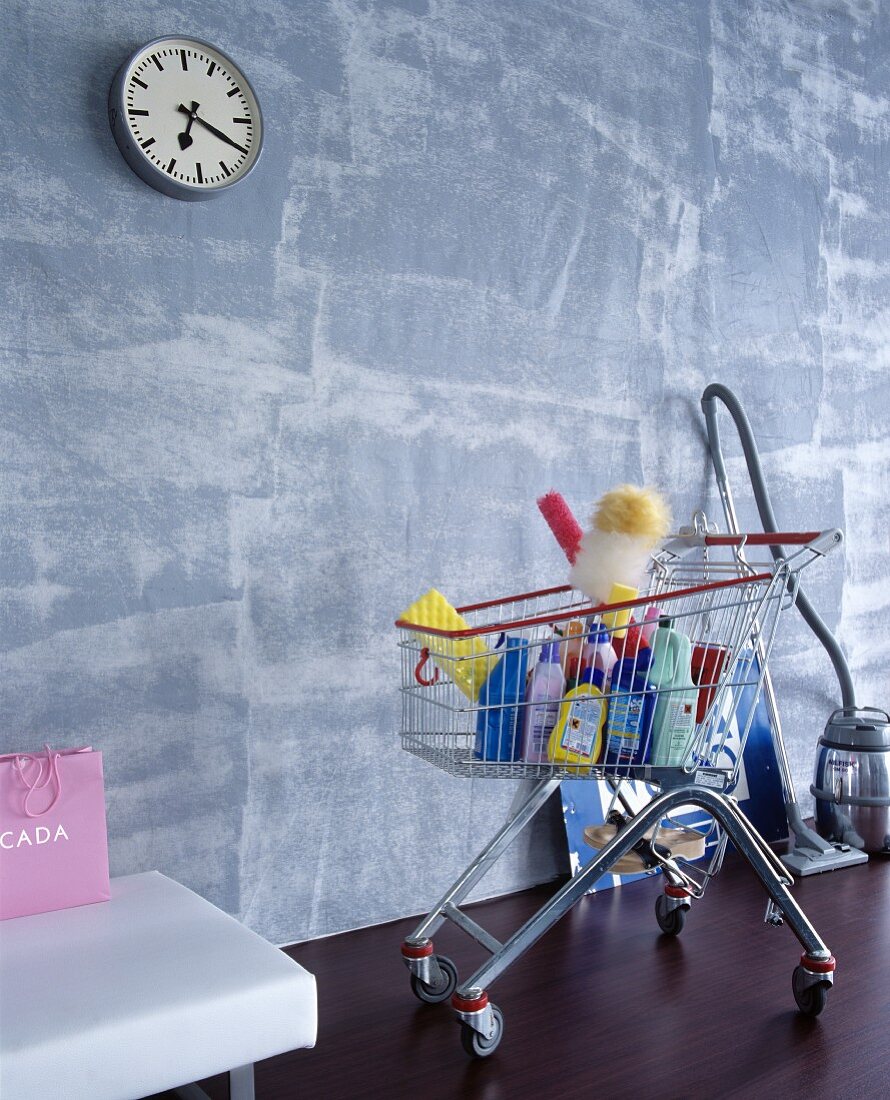 Cleaning agents in shopping trolley below clock on grey wall