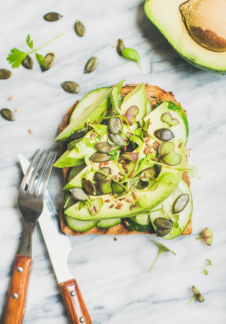 Sandwich with avocado, cucumber, kale, kress sprouts, pumpkin seeds over marble background