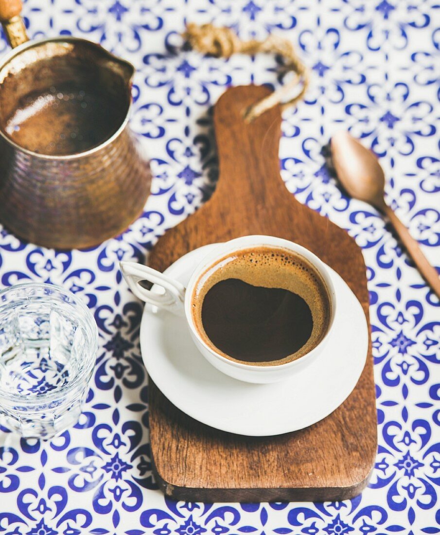 Cup of black Eastern style coffee on wooden serving board over oriental bright motley Moroccan patterned background