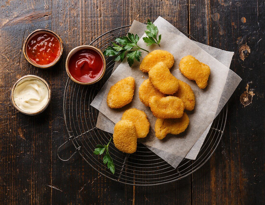 Chicken breast nuggets with popular sauces for choice on wire rack on wooden background