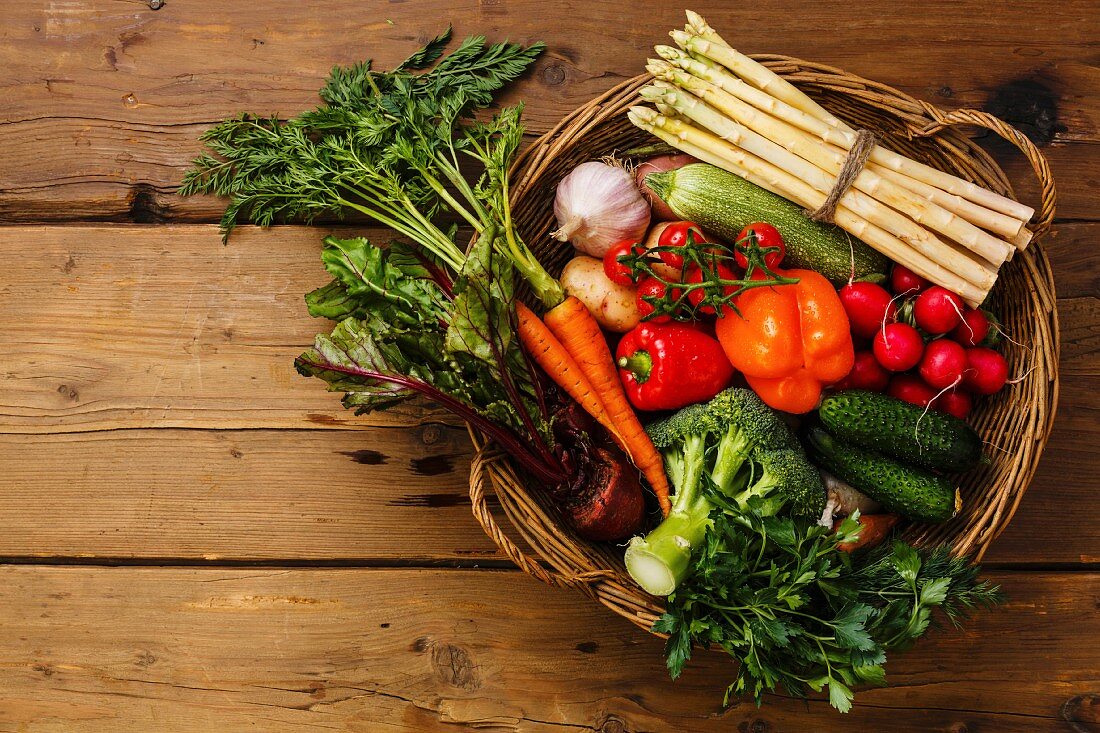 Fresh vegetables in basket on wooden background