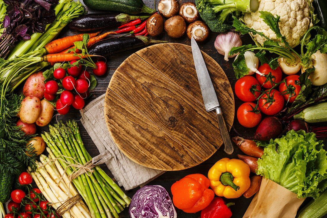 Fresh vegetables around round wooden cutting board copy space