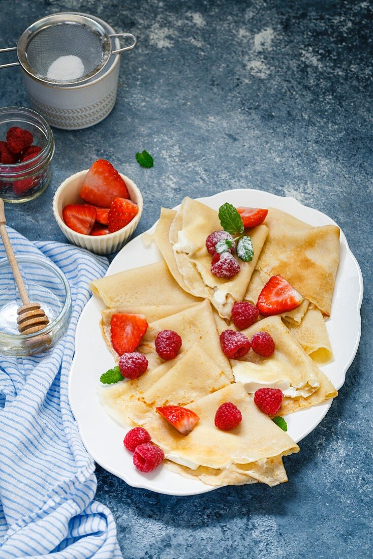 Crepes topped with cream, berries, icing sugar