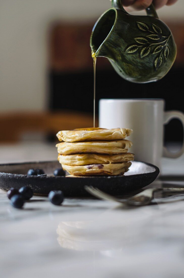 Syrup pouring from a jug onto a pile of pancakes