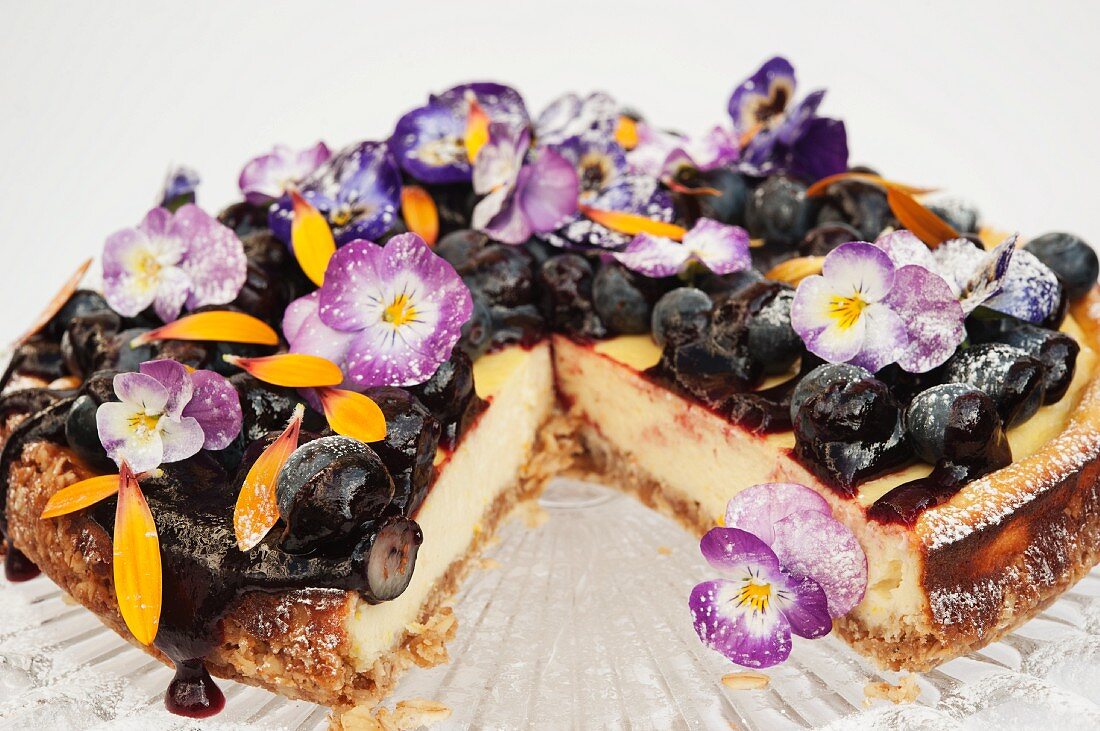 Blueberry cheese cake on a glass cake stand decorated with Pansy flowers and Marigold petals