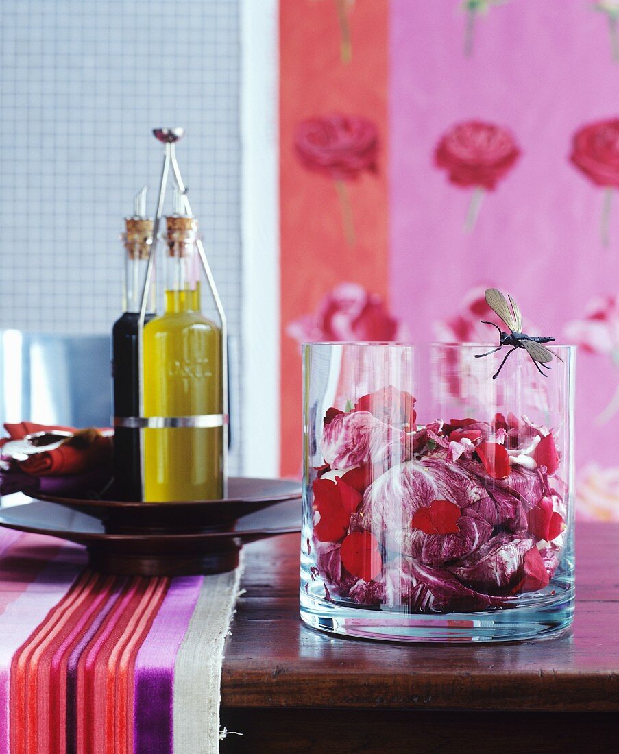 Radicchio mit Rosenblättern in Glasschale und Olivenöl auf Holztisch