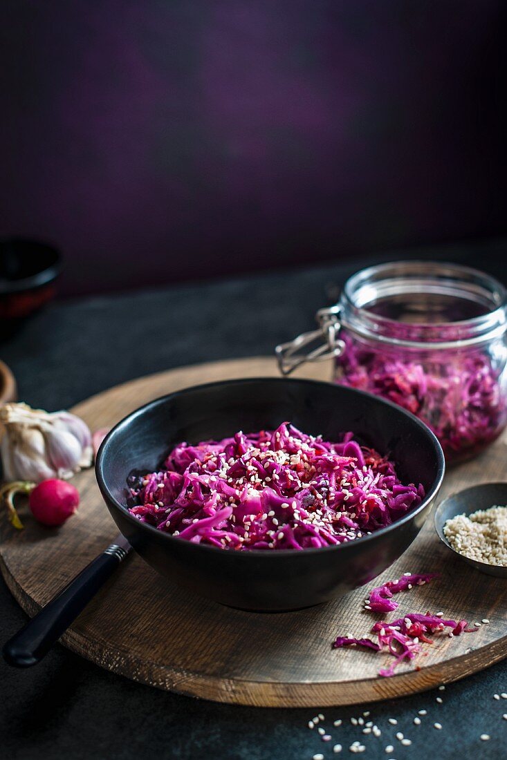 Home made red cabbage kimchi in a bowl, jar in the background