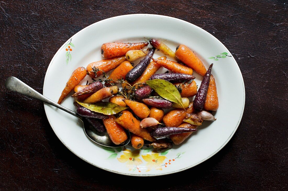 Glazed colourful carrots with garlic, laurel and thyme (top view)