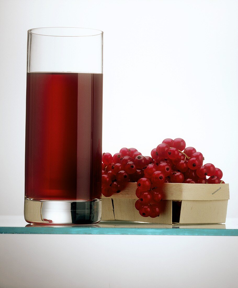 Ein Glas roter Johannisbeersaft & rote Johannisbeeren im Korb