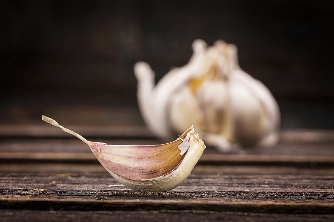 A single garlic clove in front of a bulb of garlic
