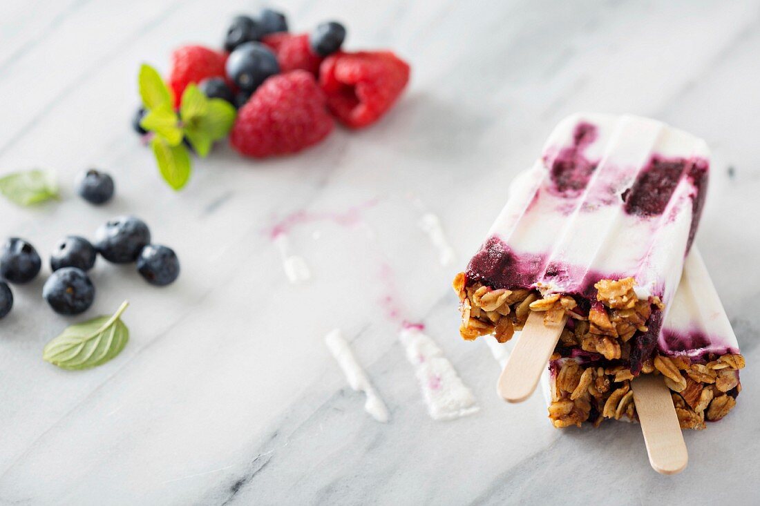 Yogurt, berry and granola breakfast popsicles on marble surface