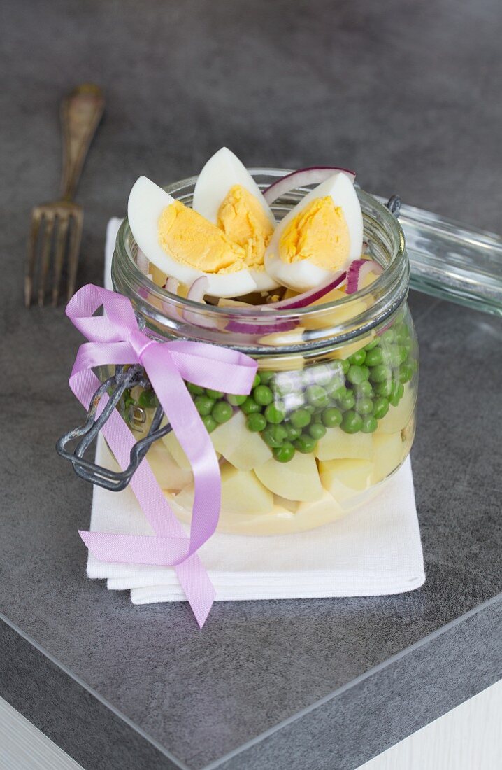 A vegetable salad with potatoes, peas, cheese, onions, mayonnaise and egg in a glass jar