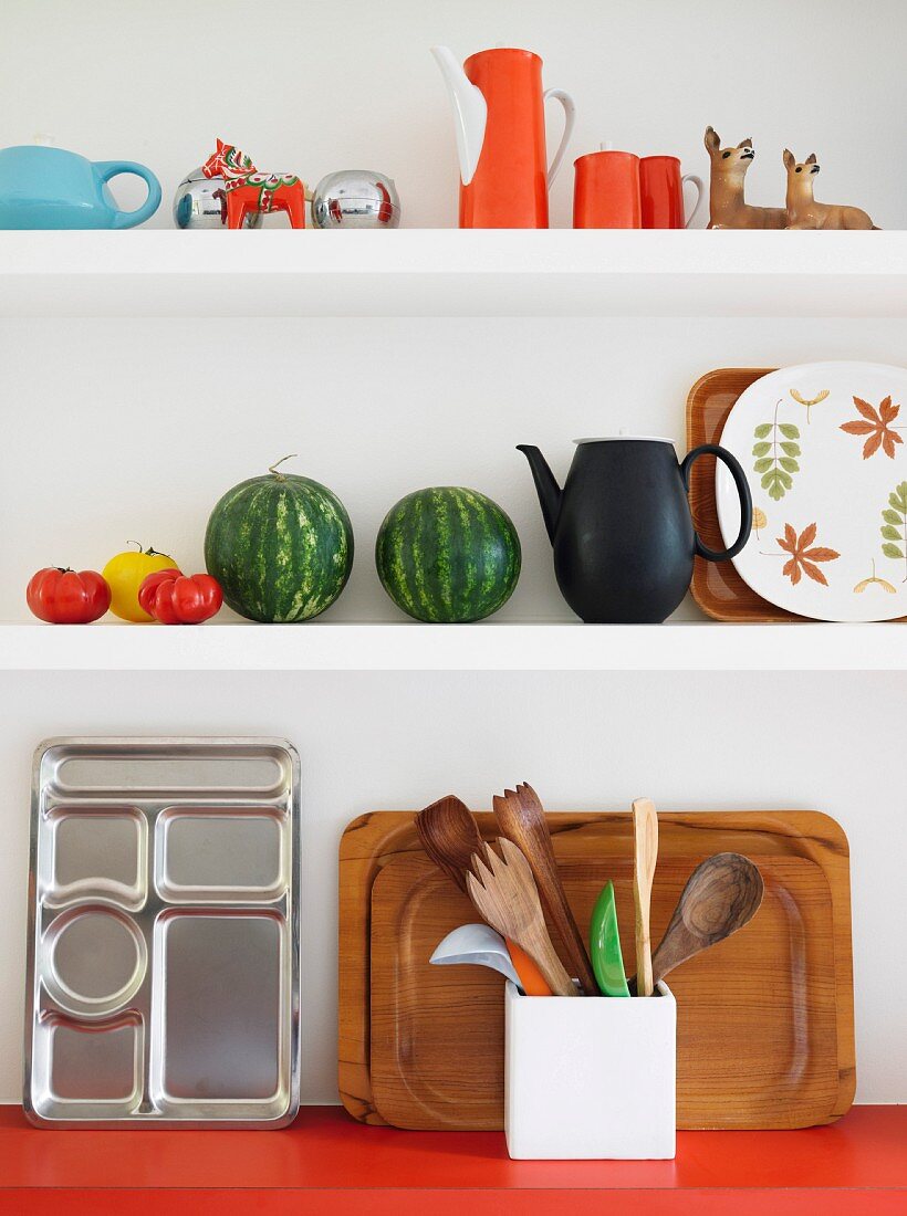 Colourful retro crockery, watermelons and trays on white kitchen shelves