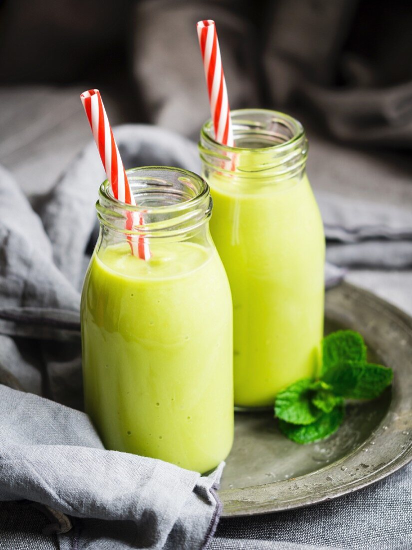 Vegan green smoothies in glass bottles with straws