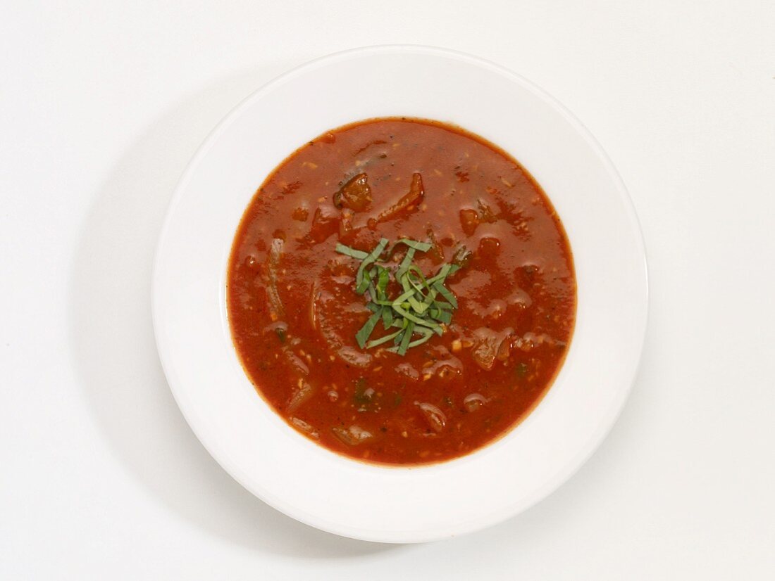 Ein Teller Tomate-Zwiebelsuppe vor weißem Hintergrund (Aufsicht)