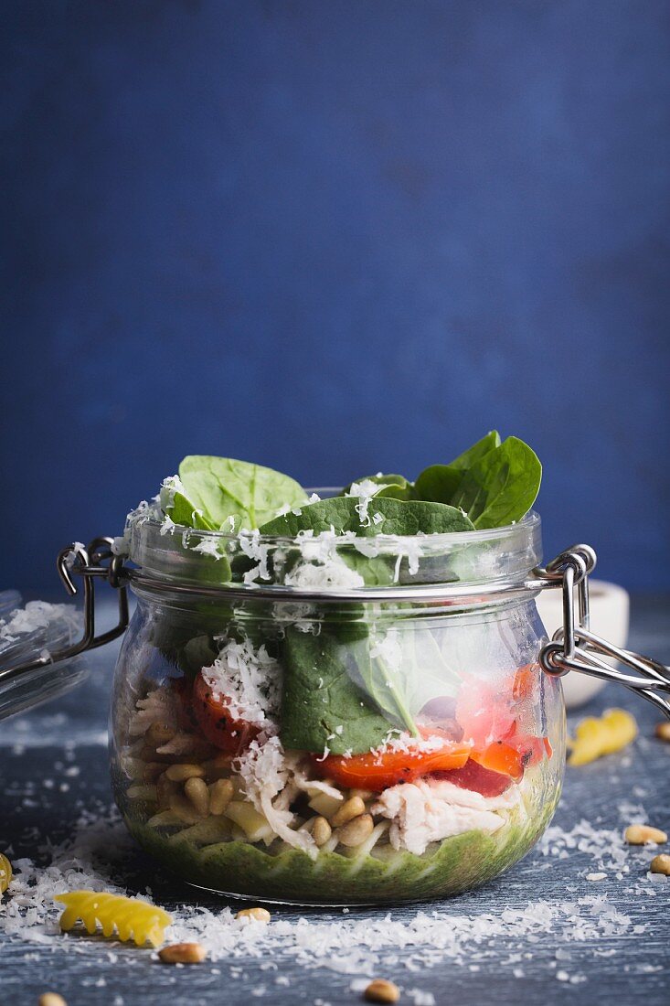 Salad with fusilli, pesto, red pepper, spinach, chicken and parmesan in a glass jar