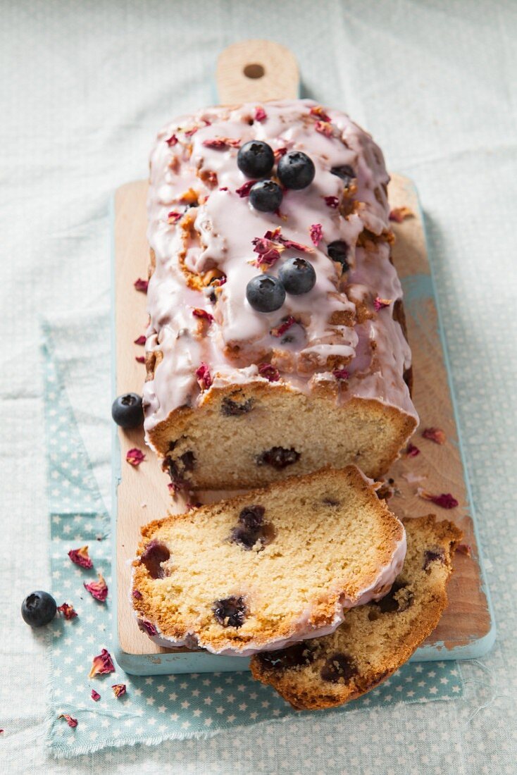 A sliced blueberry loaf cake with icing and dried rose petals