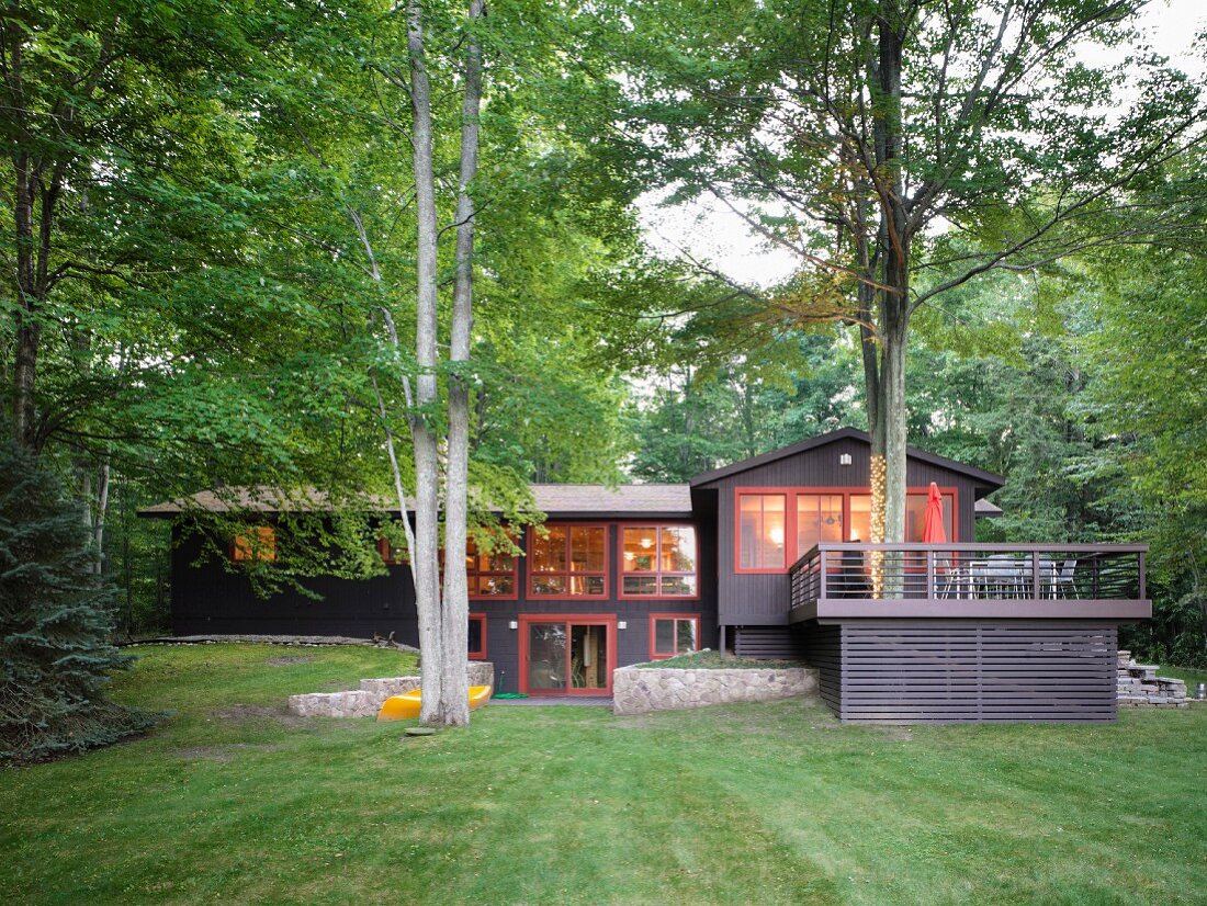 Renovated wooden house with terrace and red window frames amongst lawns