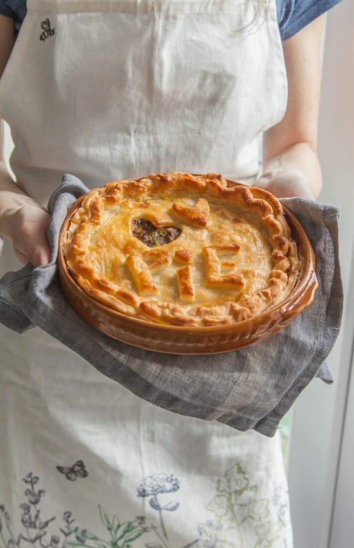 A woman holding a meat pie decorated with 'Pie' lettering and a dough heart
