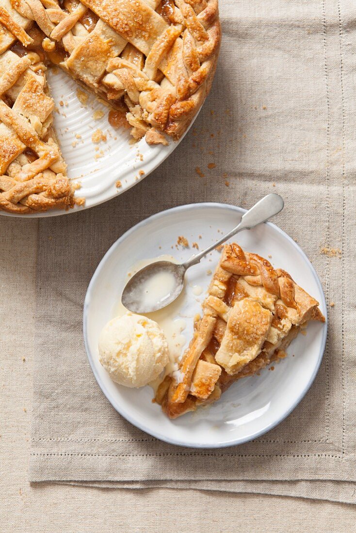 A piece of apple pie with vanilla ice cream on a plate (top view)