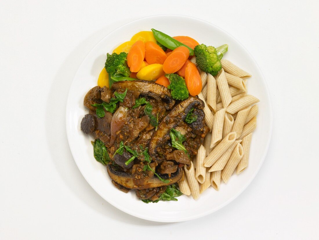 Mushroom ragu with penne and vegetables on a plate in front of a white background (seen from above)