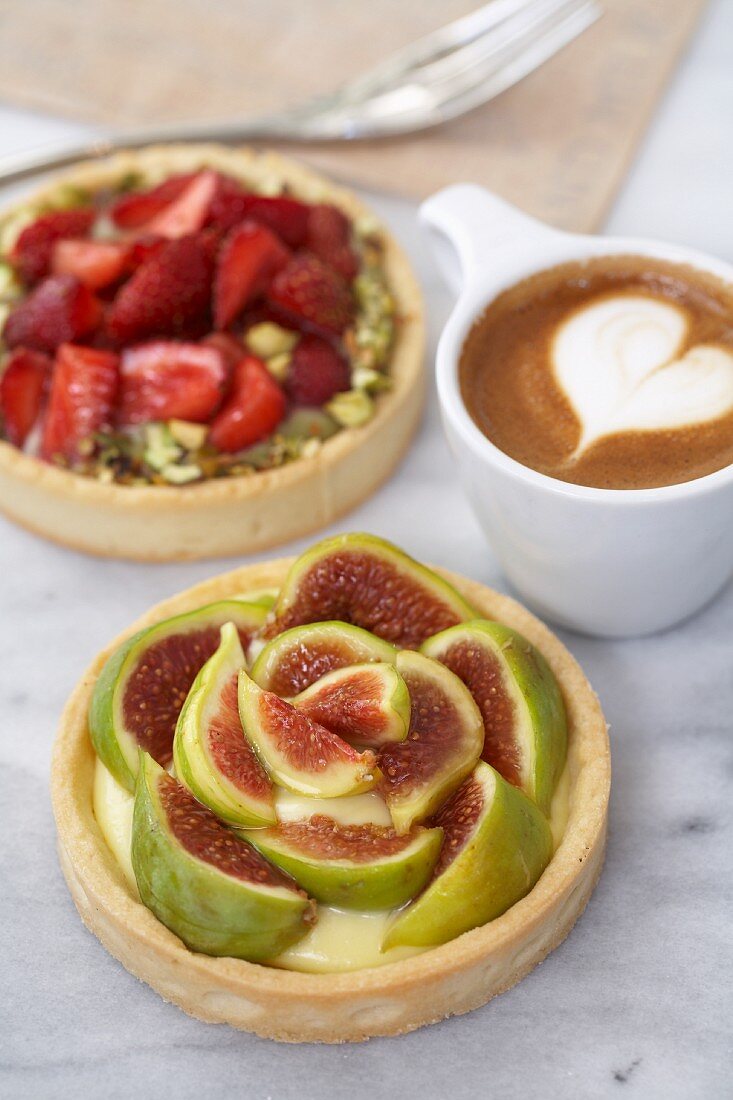 A fig tart, a strawberry tart with pistachios, and a cappuccino