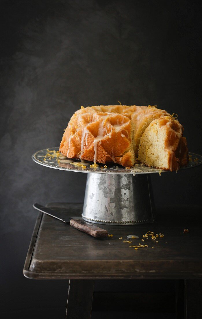 Joghurt Bundt Cake mit Zitrone auf Kuchenständer vor schwarzem Hintergrund