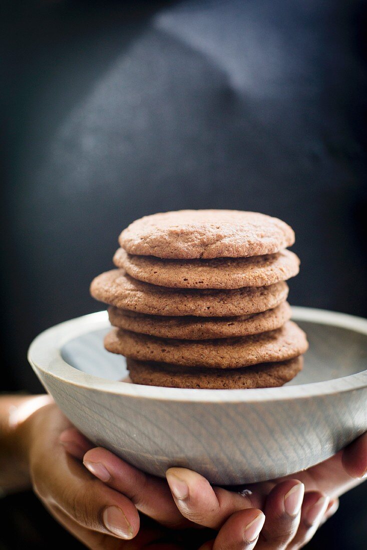 Stack of Brownie cookies in a grey wooden bowl model hands on shot