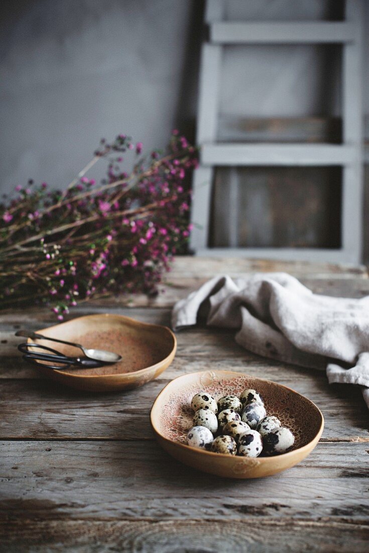 Stillleben mit Wachteleiern und Blütenzweigen auf rustikalem Holztisch in Landhausküche