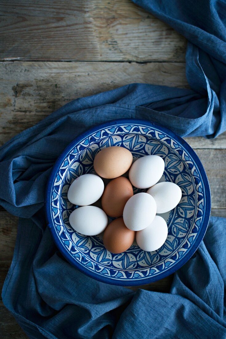 Frische Hühnereier in blau-weisser Keramikschale auf Holztisch (Aufsicht)