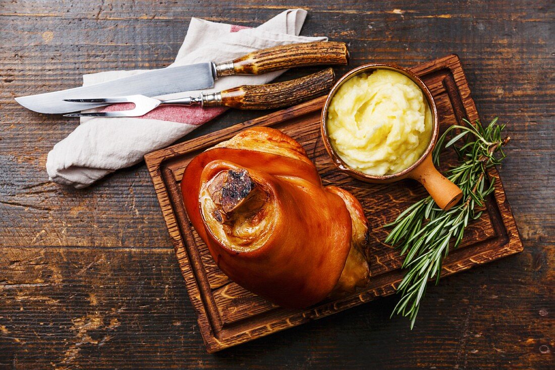 Schweinshaxe mit Kartoffelpüree auf Holzbrett (Bayern, Deutschland)