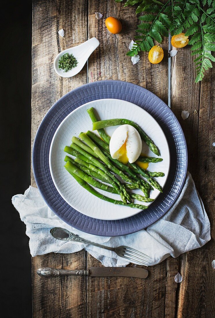 Asparagus and egg on white plate over wooden table