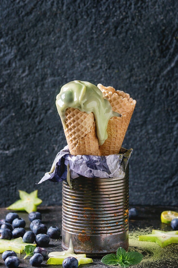 Waffle cones of Green tea matcha soft elastic ice cream with mint leaves, carambola, lime, blueberries in old tin can