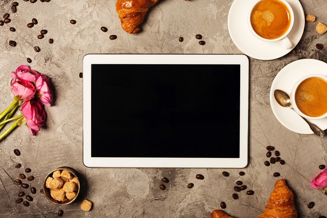 Tablet, coffee and croissants on grey stone background