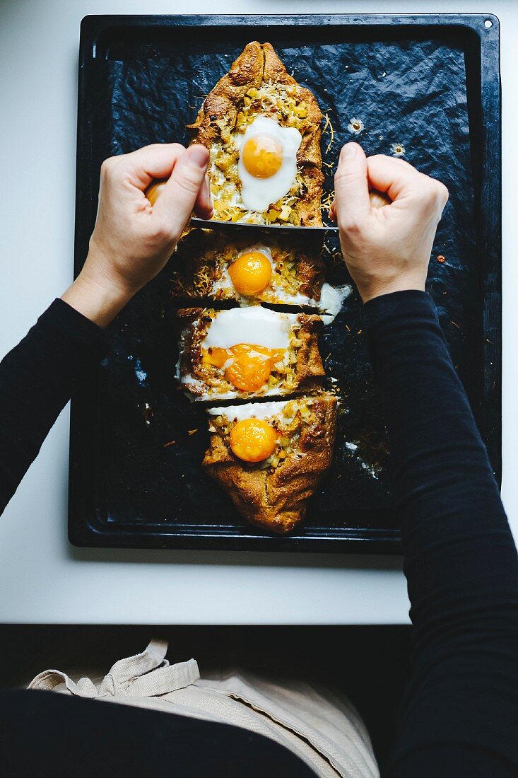 Person schneidet Eier-Kartoffelkuchen auf Backblech in Stücke