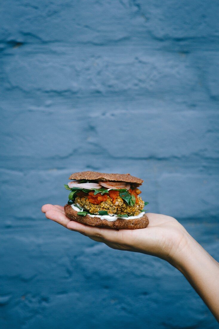 Veganer Burger mit Tomatensalsa auf Handfläche vor blauem Hintergrund