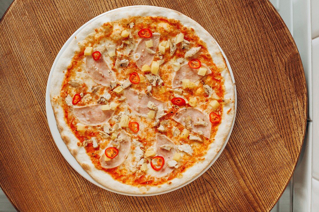 Pizza with ham, pineapple and chillies on a wooden board (top view)