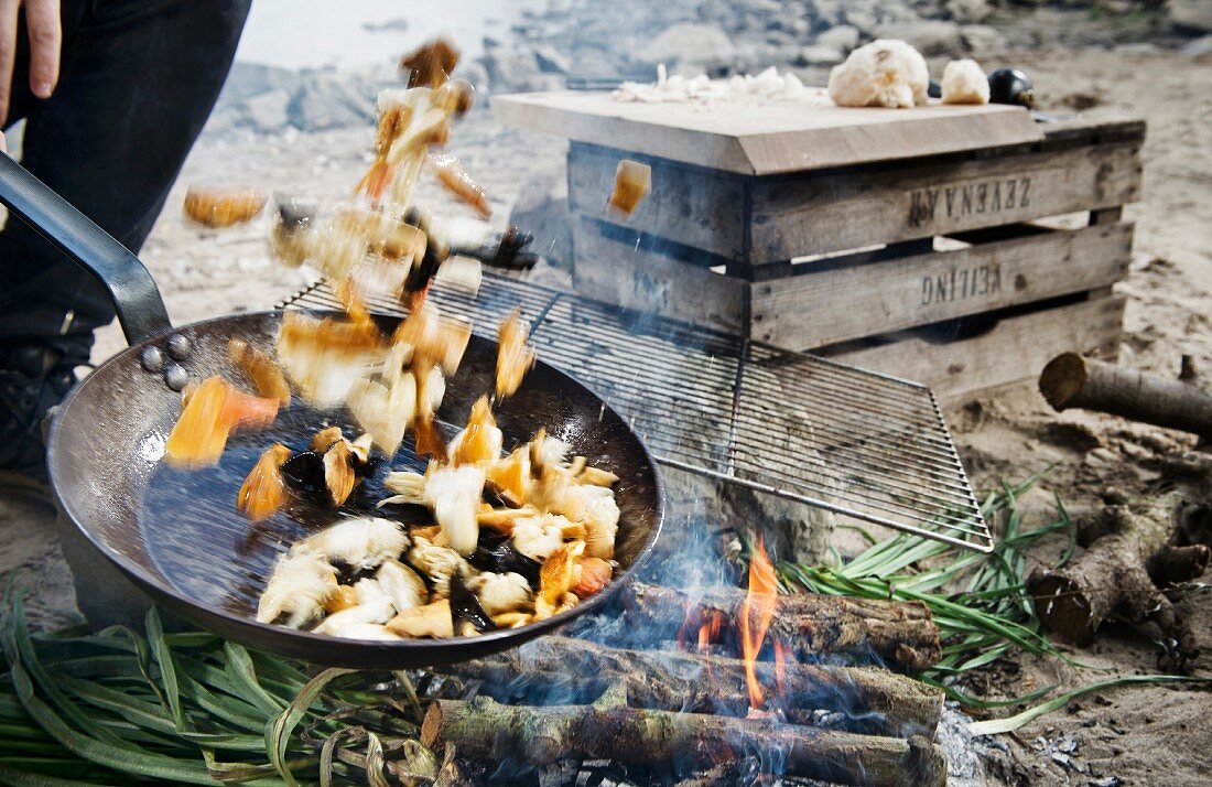Camping-Essen in Pfanne wird über Lagerfeuer geschwenkt