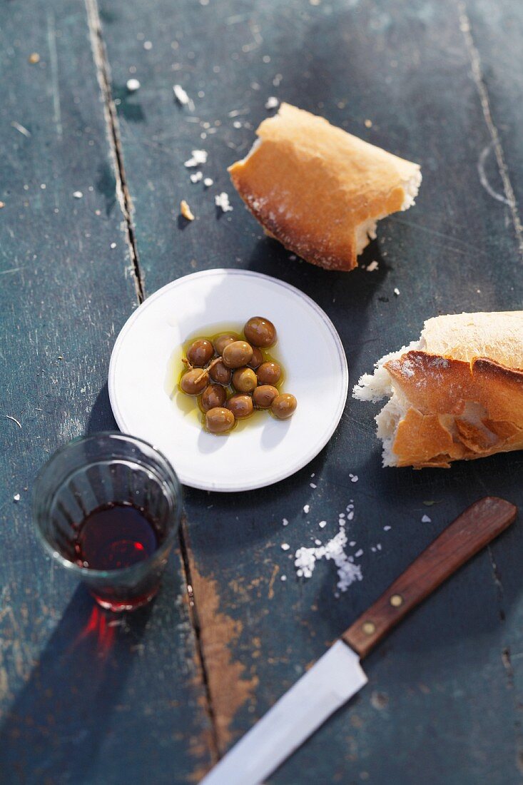 Oliven mit Brot und einem Glas Rotwein auf rustikalem Holztisch