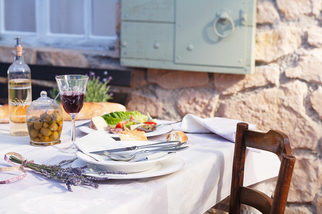 Gedeckter Terrassentisch mit Oliven, Brot und Wein (Provence, Frankreich)