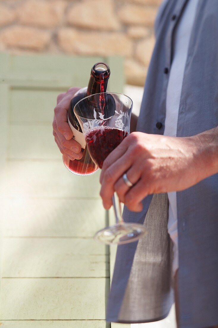A man pouring red wine from a bottle into a glass