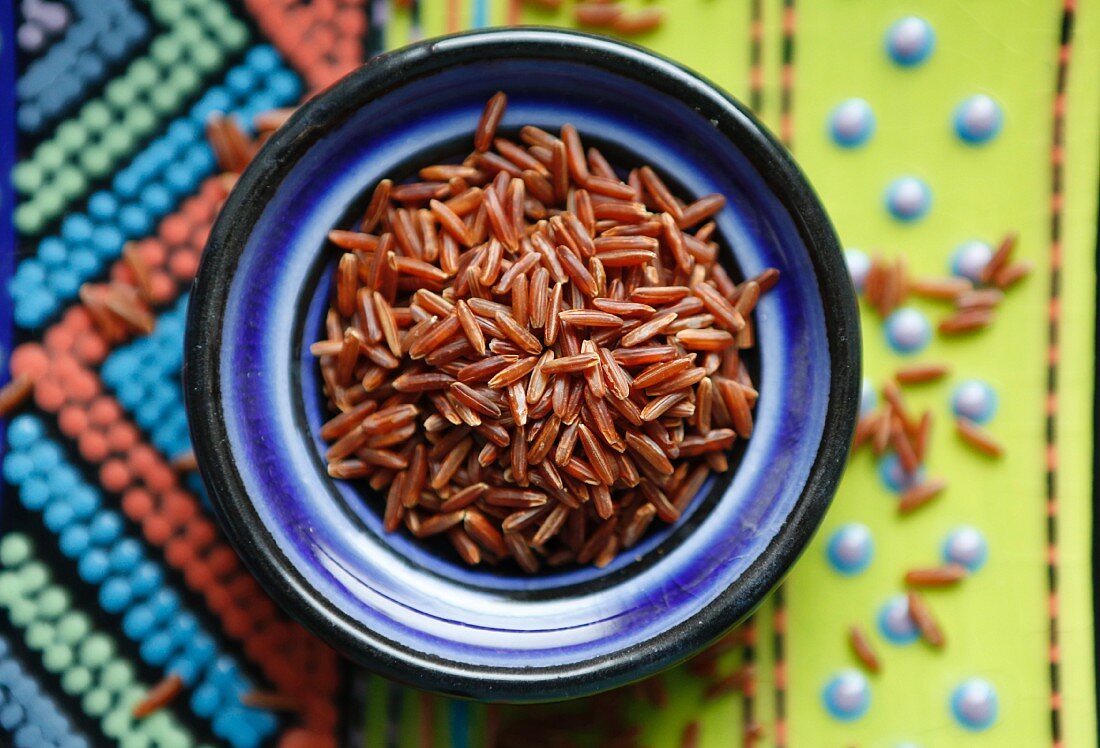 Red rice in a bowl on a colourful background (seen from above)