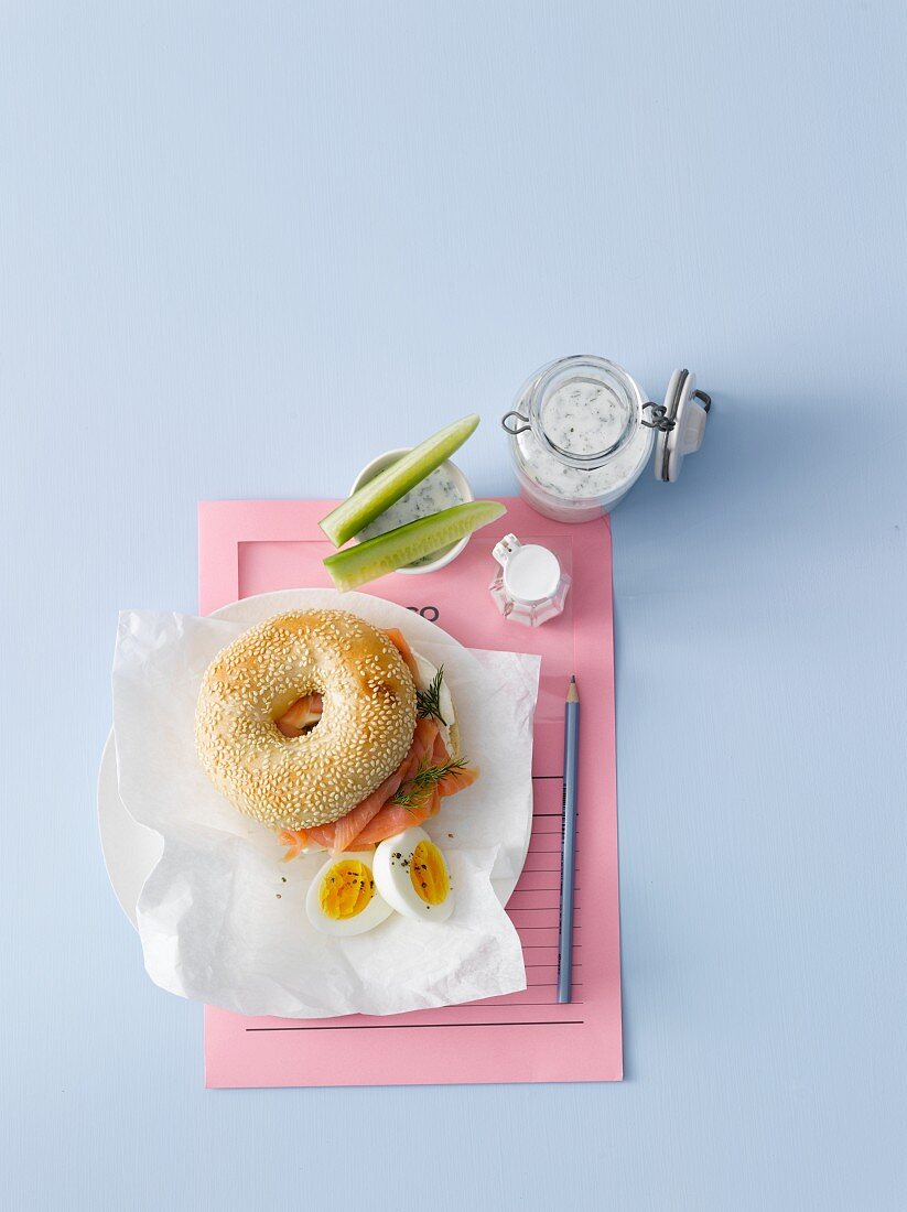 A sesame bagel with smoked salmon, dill, horseradish cream cheese, a hard-boiled egg and sour milk with herbs and cucumber