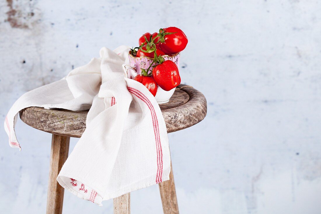 Small plum tomatoes on a wooden stool with a tea towel